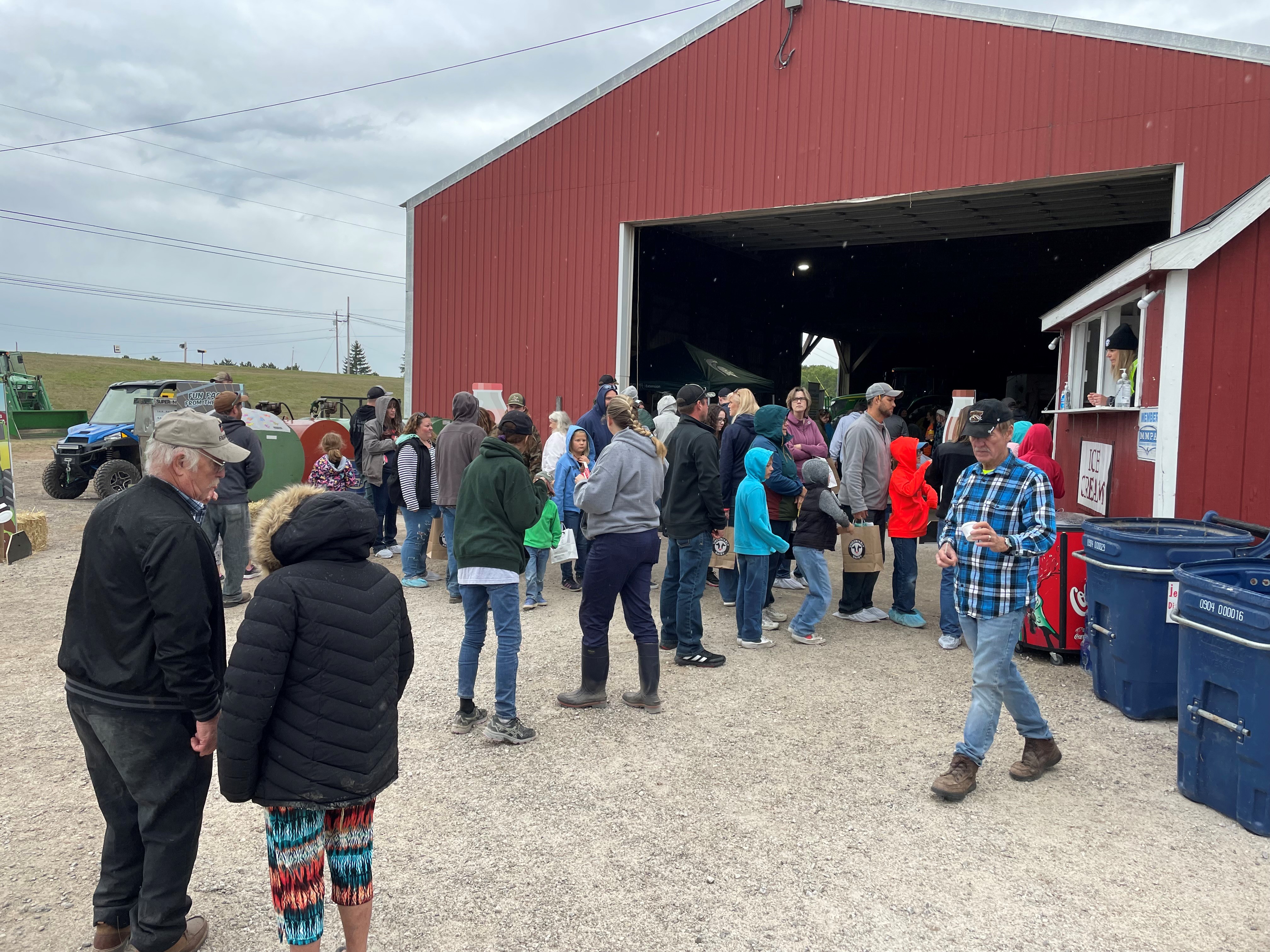 People standing in line outside of a red barn.